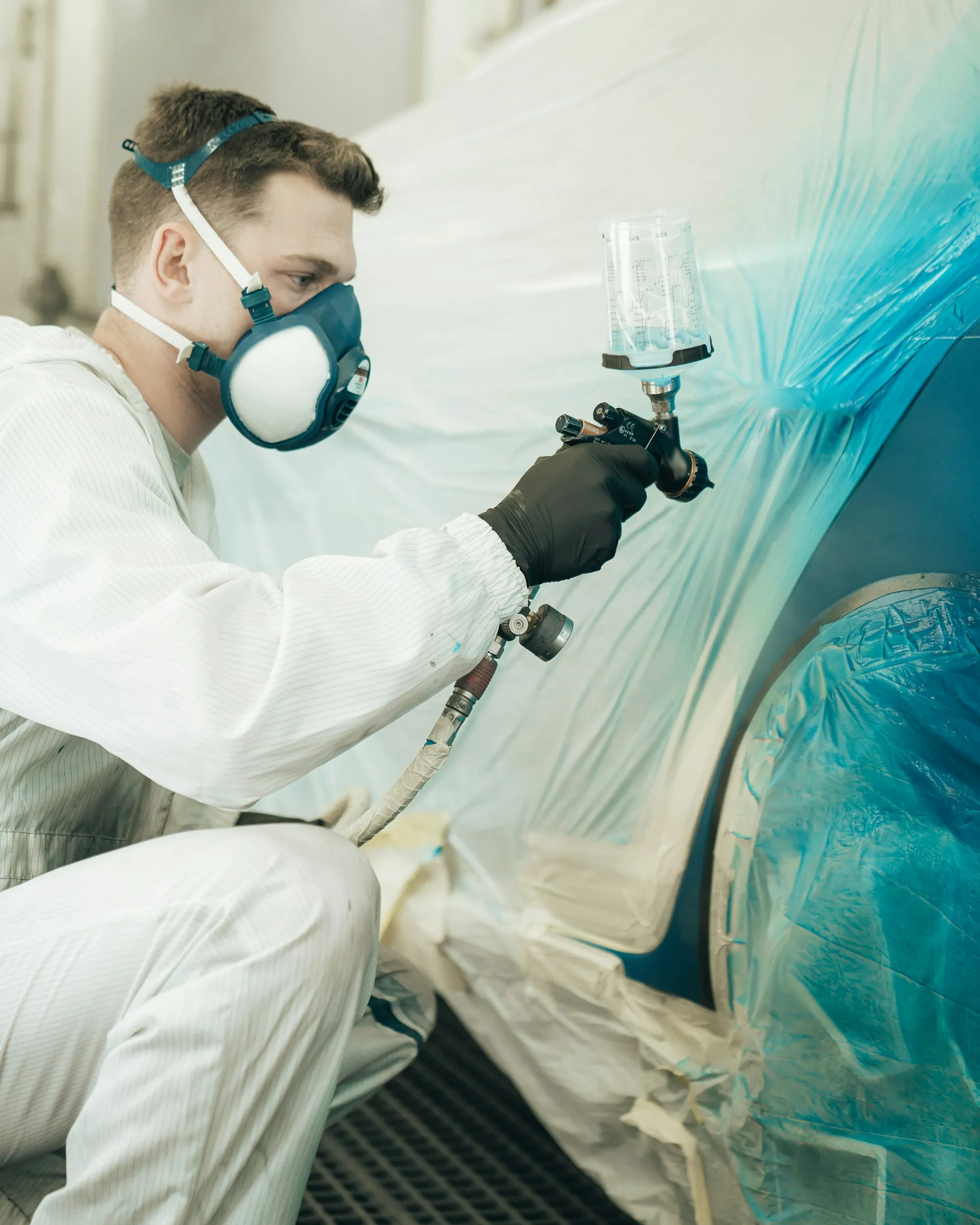 Painter in a protective suit spraying a car