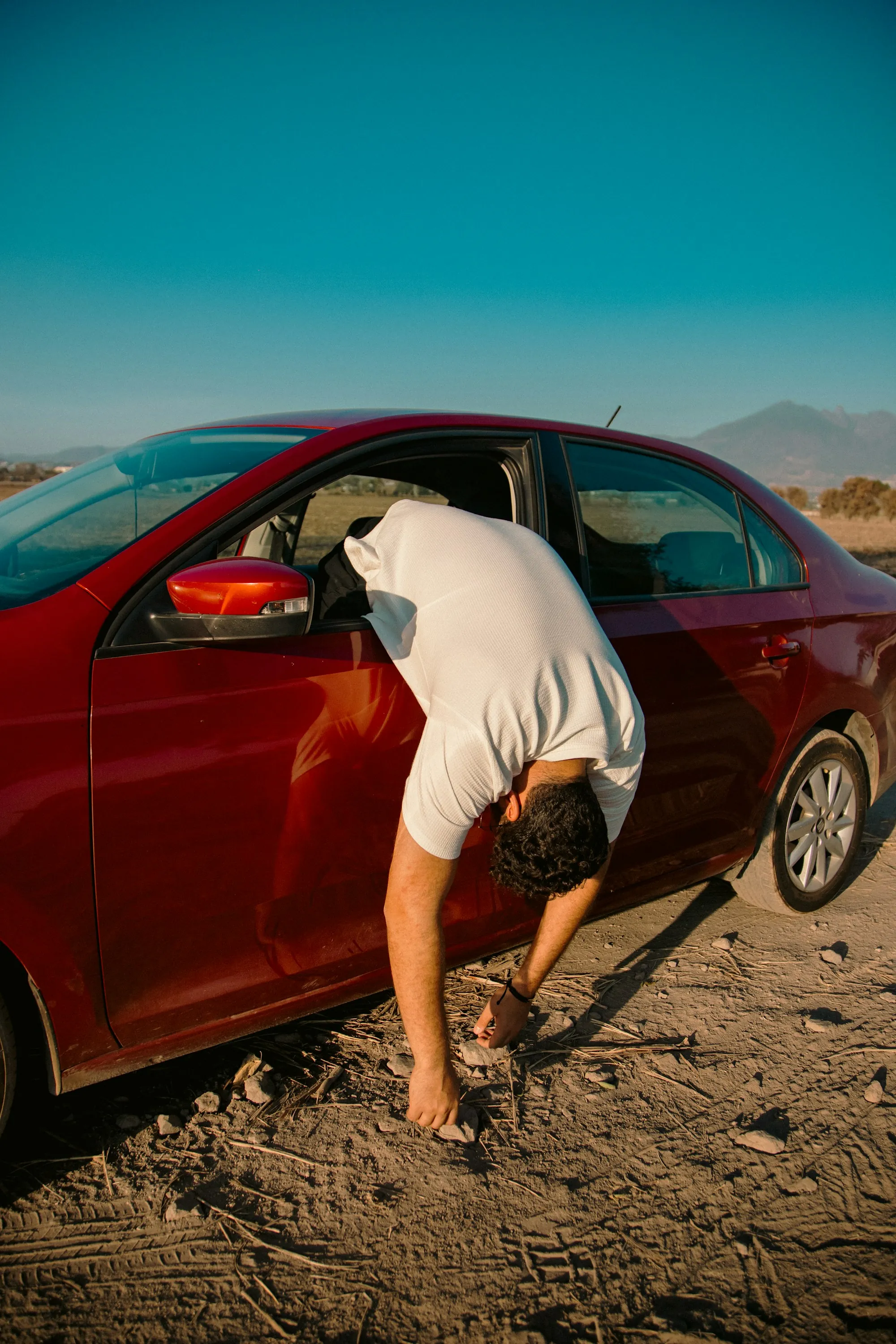 Technician fitting a repaired front fender to a white sedan in a body shop bay