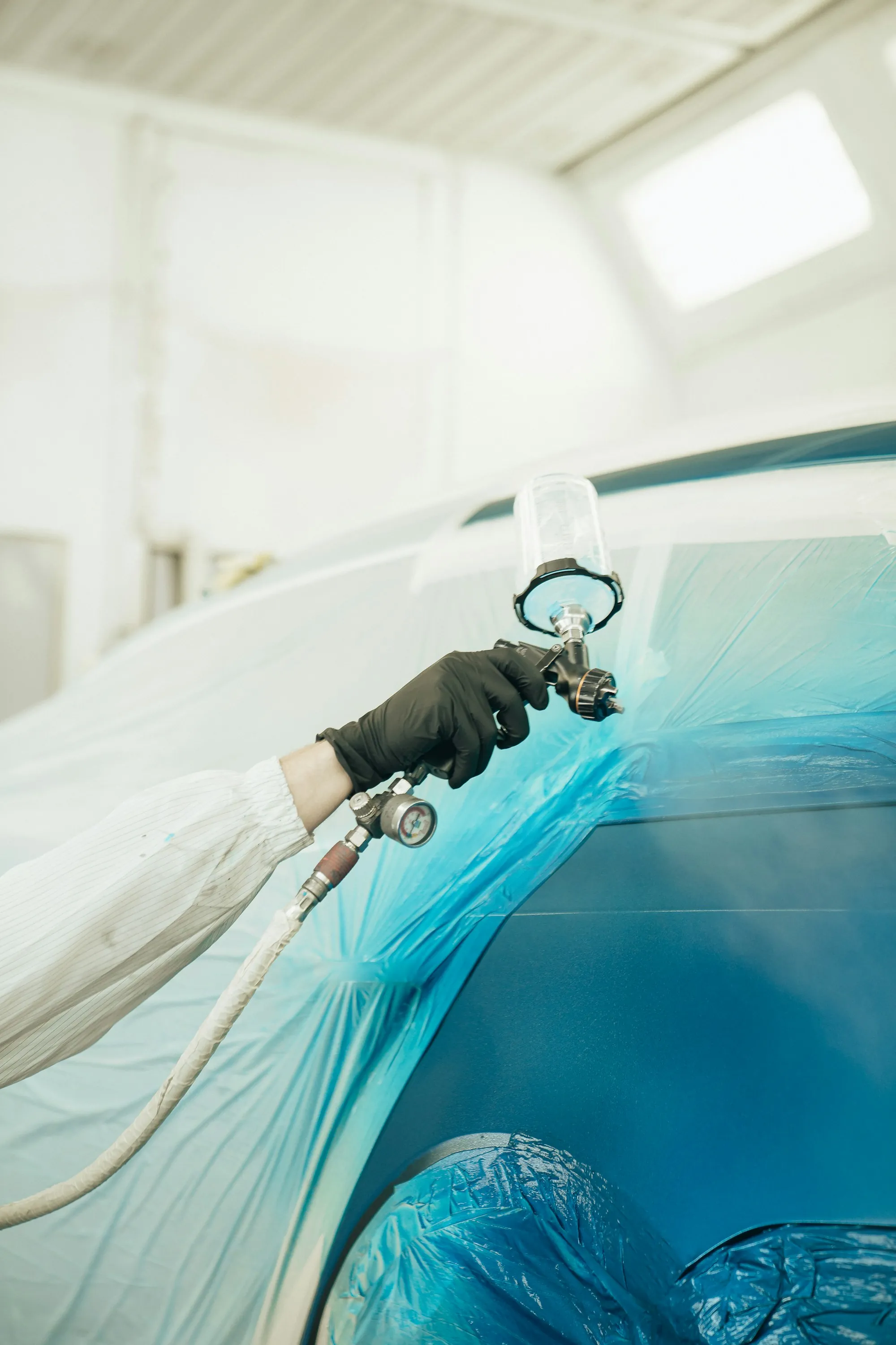 Painter in a protective suit spraying a primed car door inside a downdraft paint booth