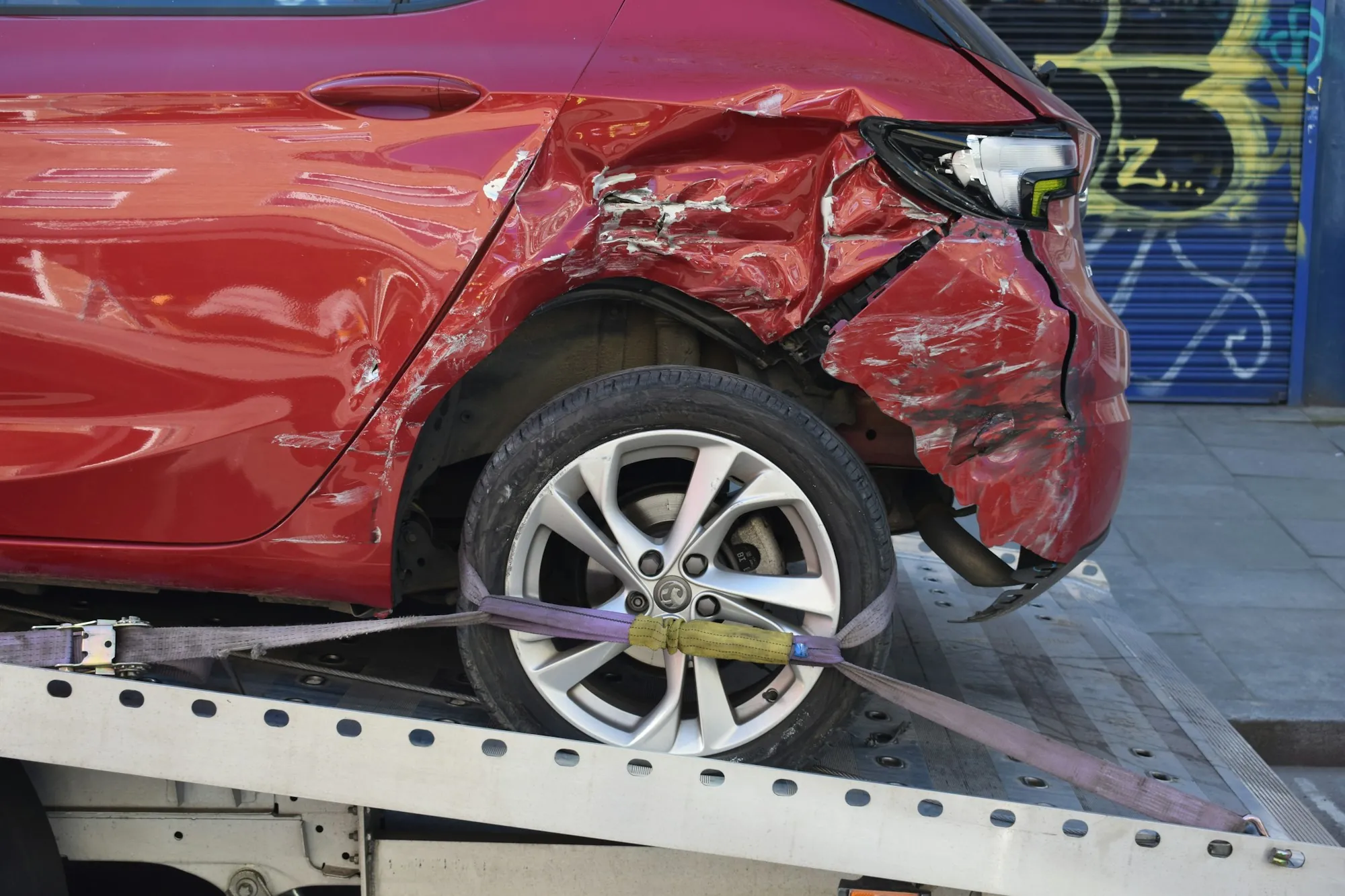 Gray crossover with a crushed front fender and headlamp waiting in a collision repair bay